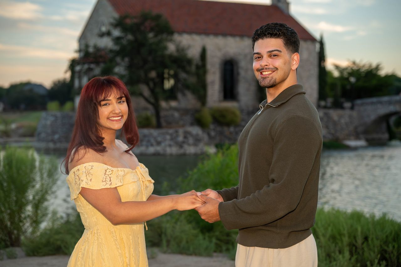 Luca and Ana hold hands and smile at the camera by the chapel