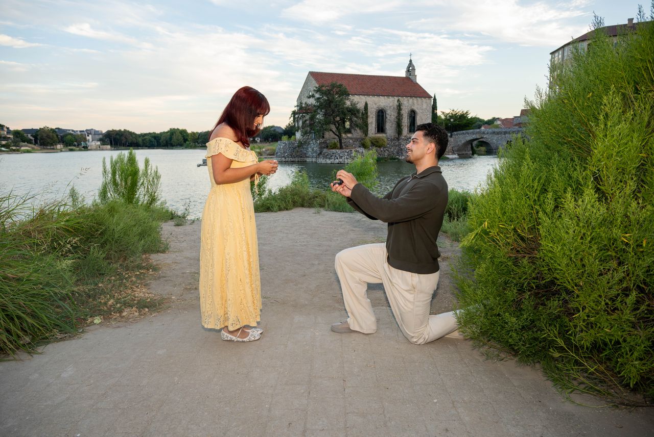 Luca kneels on the path and holds up the ring to Ana