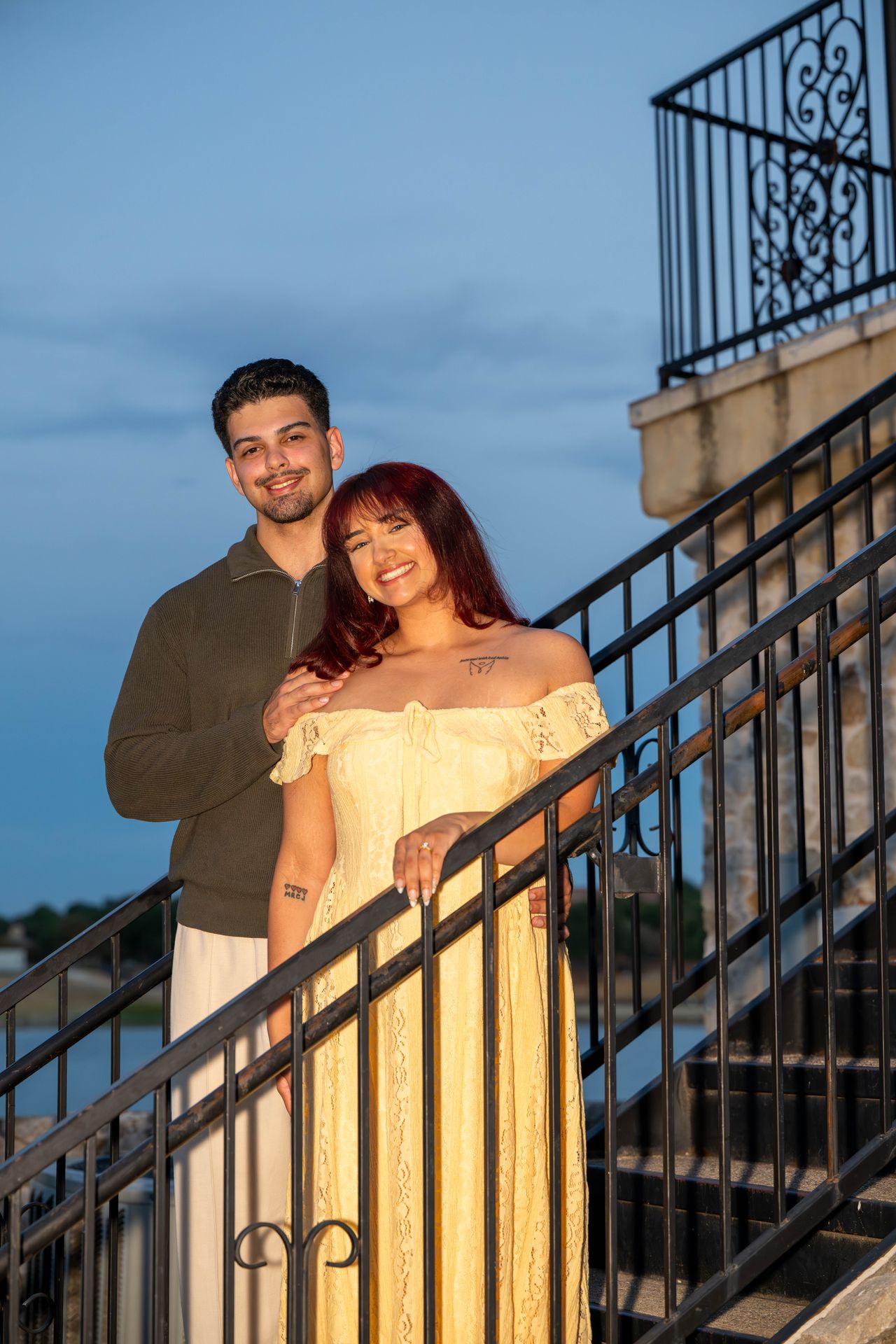 Luca and Ana smile on an iron staircase at dusk
