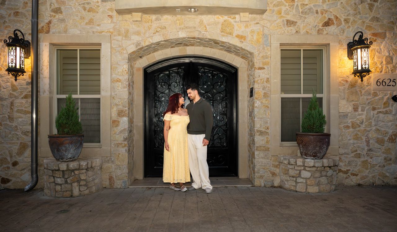Luca and Ana look at each other at an arched iron door between two lanterns