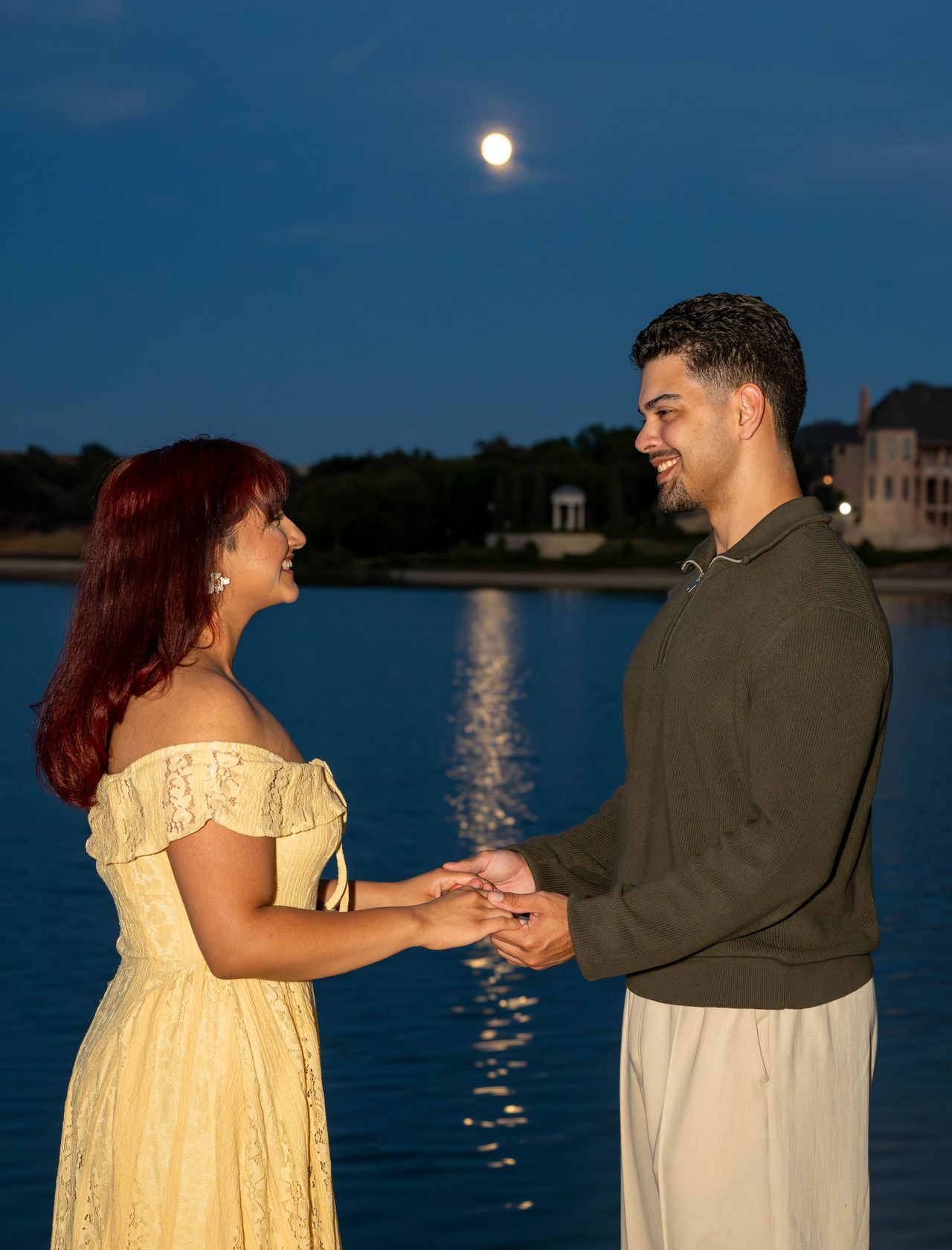 Luca and Ana hold hands, the moon reflected on the water