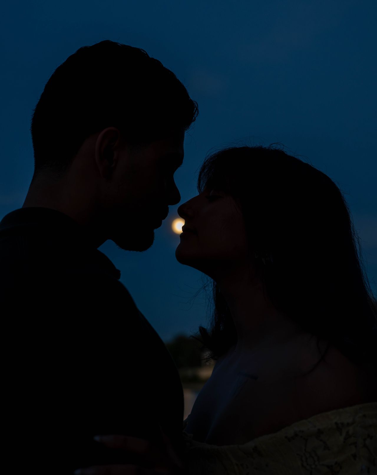 Luca and Ana in silhouette, about to kiss, the moon between their faces