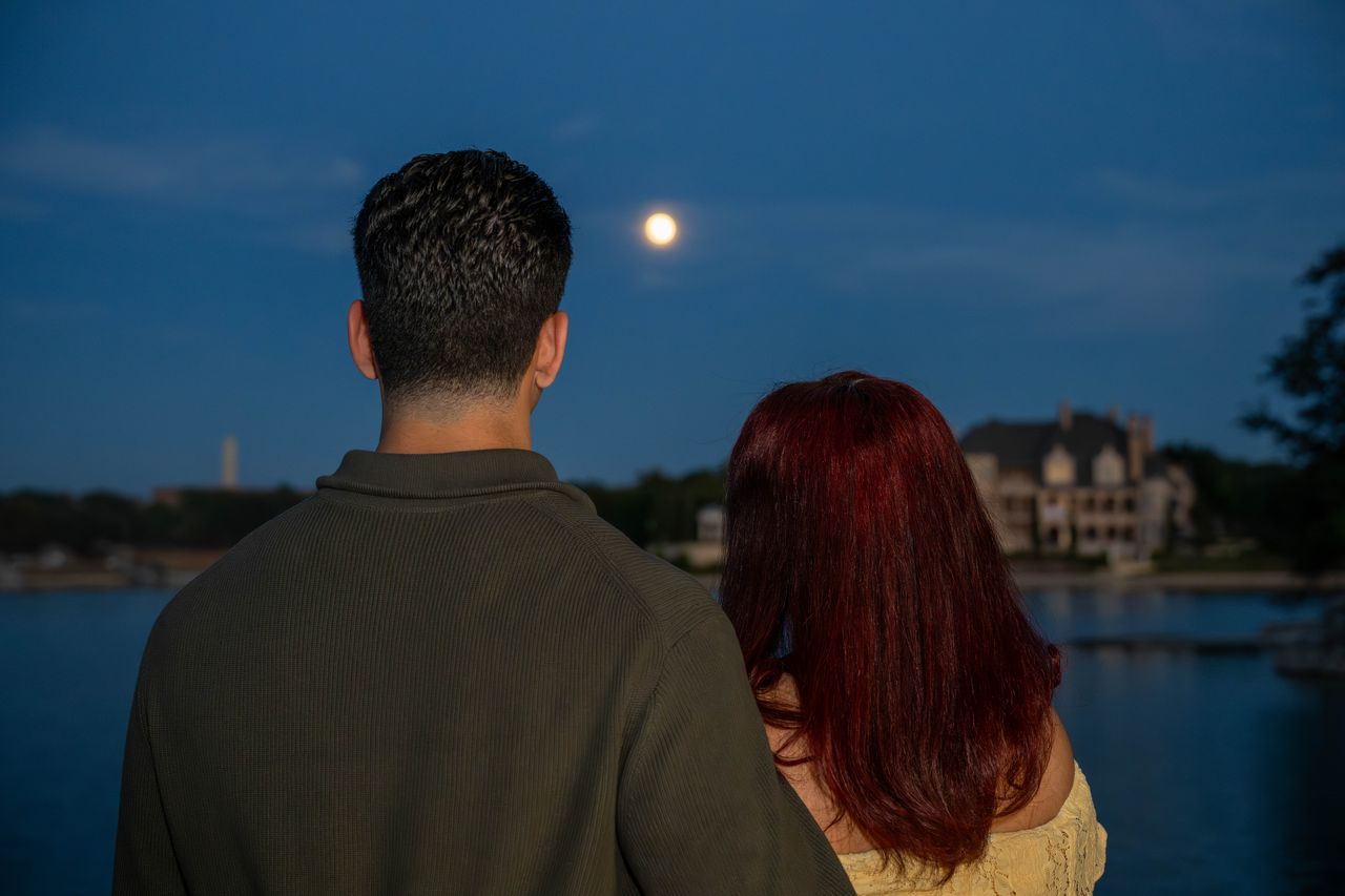 Luca and Ana seen from behind, looking at the moon over the lake