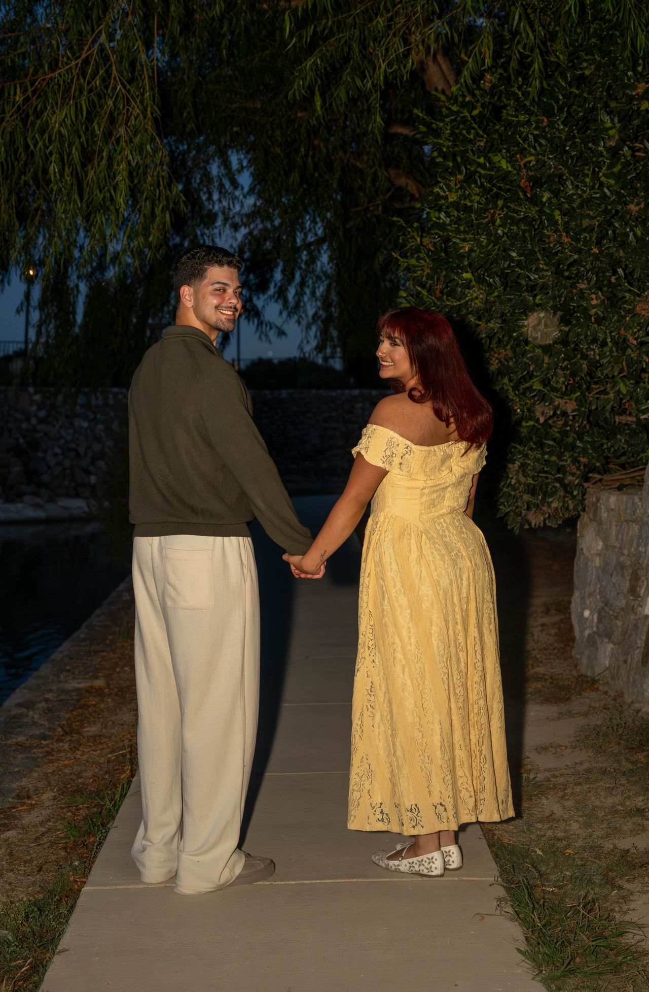 Luca and Ana hold hands on a path under the trees