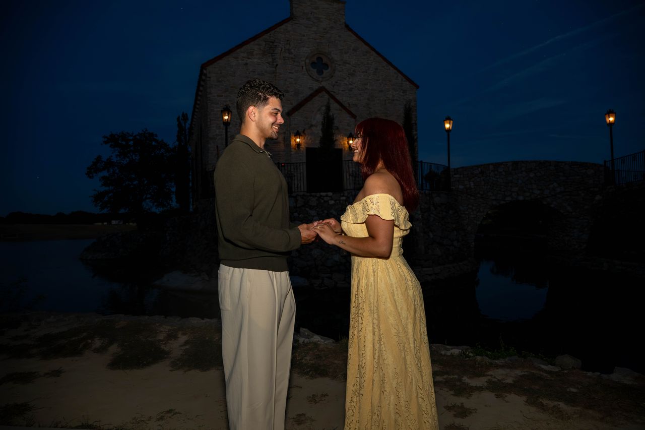 Luca and Ana hold hands and face each other in front of the chapel at night