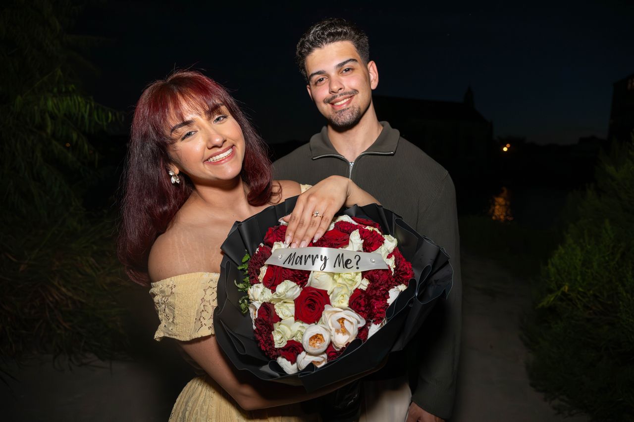 Ana and Luca smile at the camera with the Marry Me bouquet